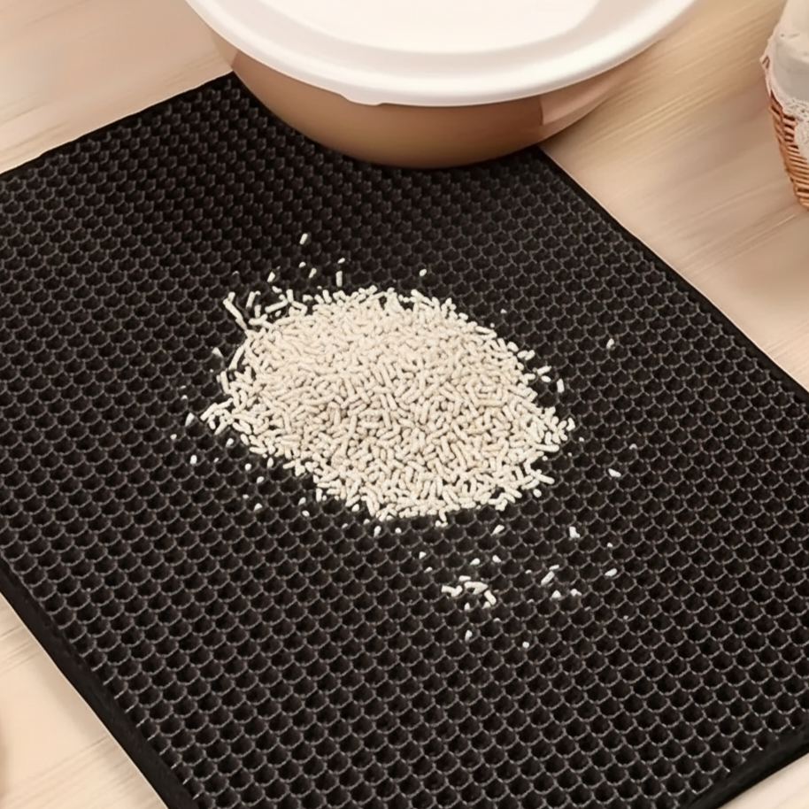 "Un tapis de litière pour chat noir avec un motif en nid d'abeille, retenant visiblement des granulés de litière blancs près d'une gamelle, illustrant son efficacité à contenir les débris.