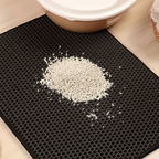 "Un tapis de litière pour chat noir avec un motif en nid d'abeille, retenant visiblement des granulés de litière blancs près d'une gamelle, illustrant son efficacité à contenir les débris.