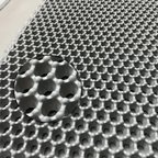 Vue rapprochée de la texture d'un tapis gris anti-dérapant, mettant en évidence le motif en nid d'abeille avec un effet de loupe qui accentue chaque cellule, idéal pour retenir les débris.